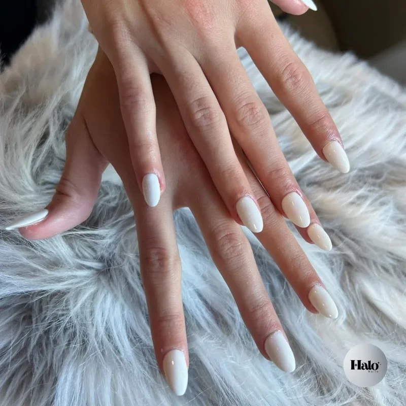 A white almond manicure resting on white fur, with the Halo Nails badge, photographed at Halo Nails Spa.
